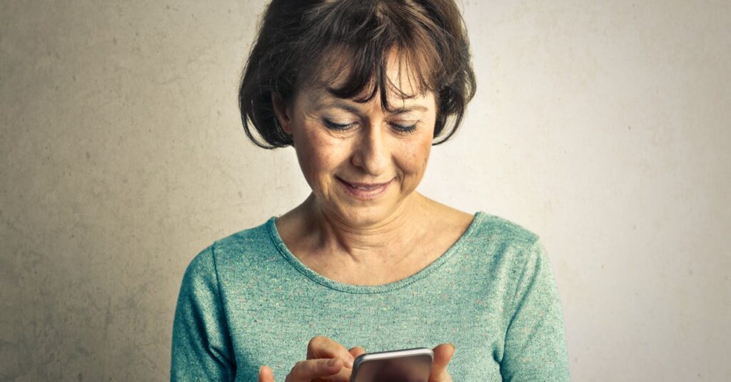 A senior woman smiling as she interacts with her smartphone indoors, expressing happiness and technology use.